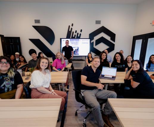 A group of people, in a class, looking backwards and smiling to the camera